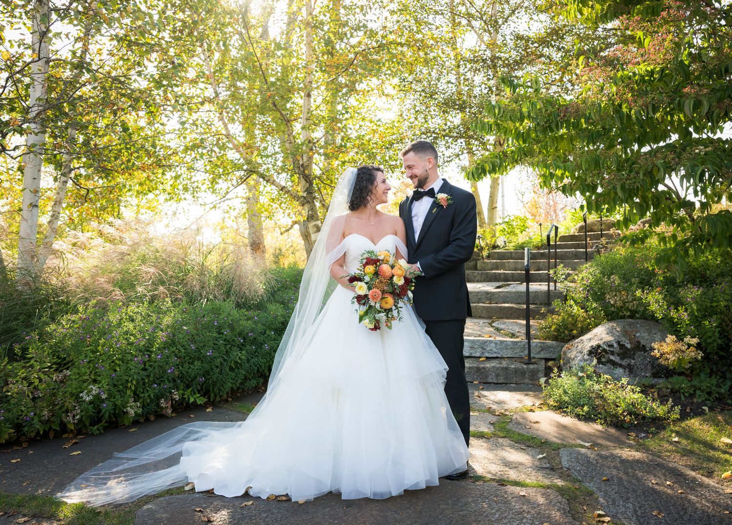 Newlywed couple poses for romantic sunset photos in a garden setting with golden light filtering through trees.