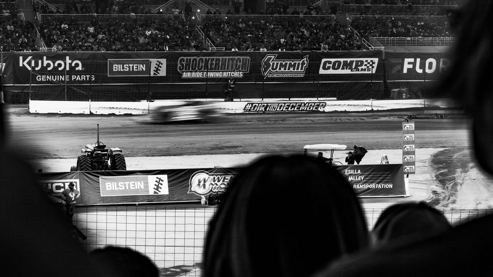 Racing track barriers and sponsor logos visible at a motorsports venue under lighting.