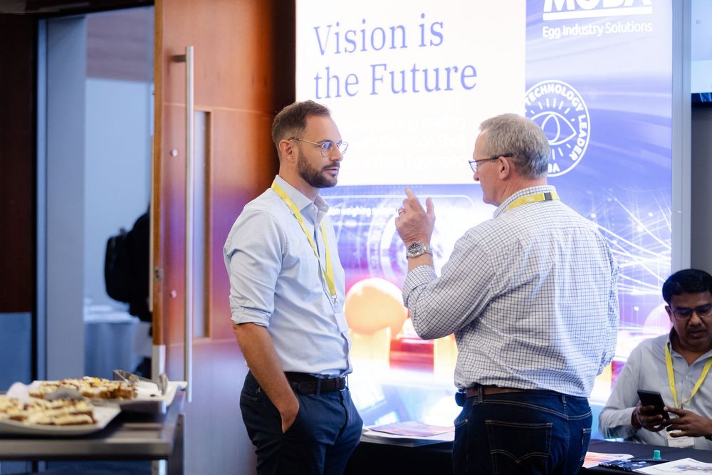 People collaborate in a professional setting with presentation screens visible in the background.