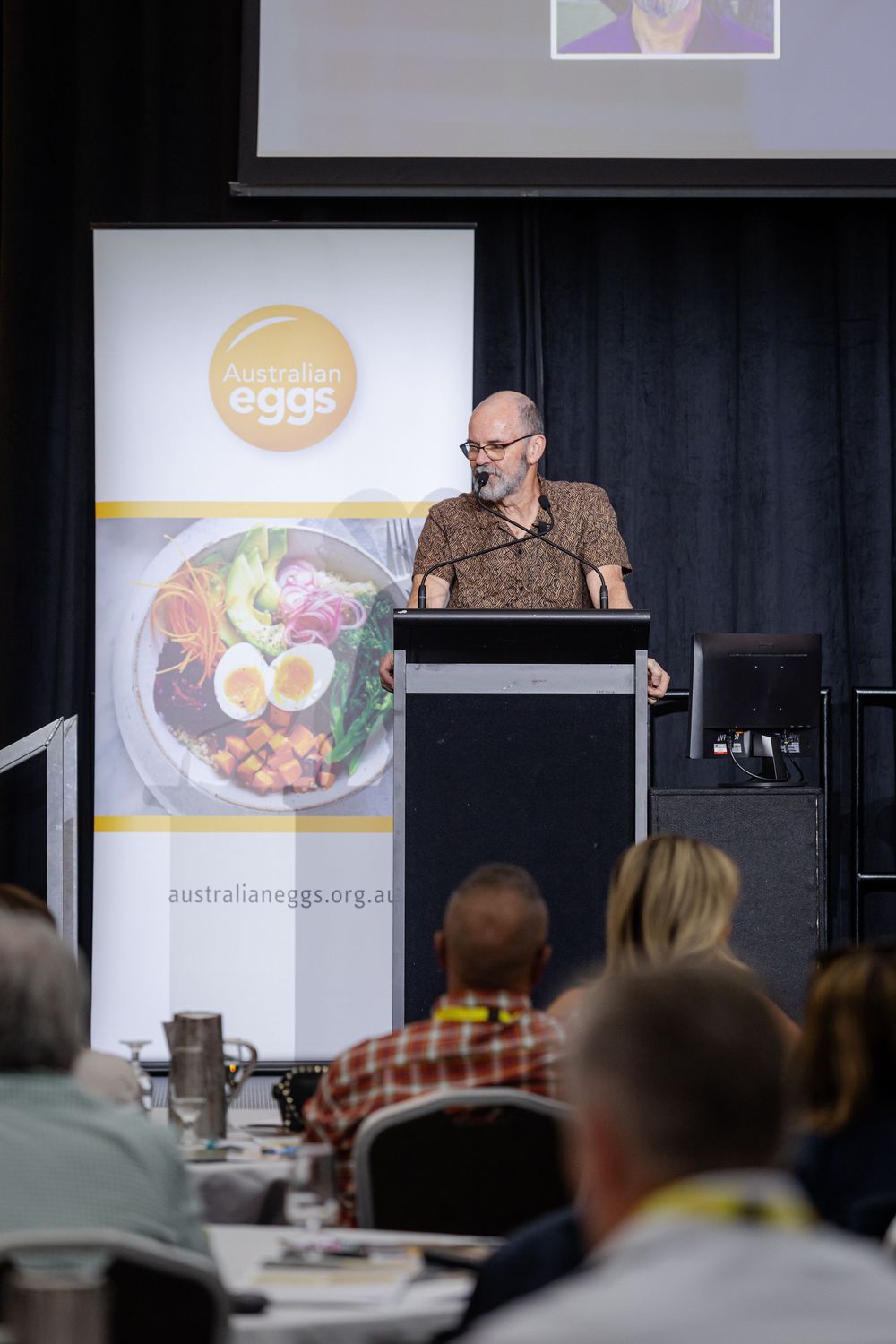 A presenter speaks at the Australian Egg Industry Forum 2022 with food presentation slides displayed on screen.