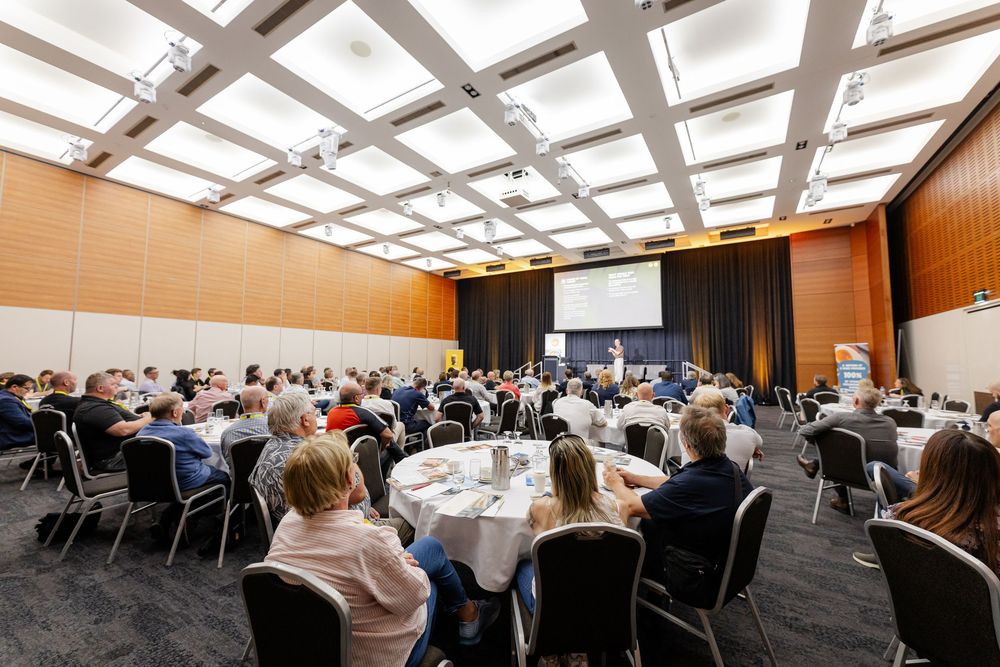 Conference room with modern skylight ceiling panels and rows of tables set up for a large business meeting.