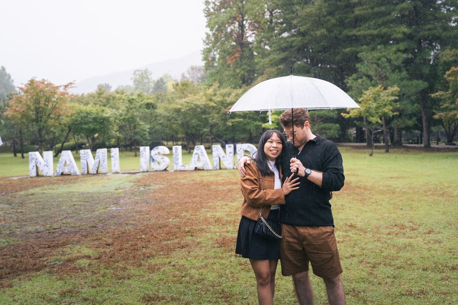 Couple sharing romantic moments in a park during autumn with white umbrella and fall foliage in background.