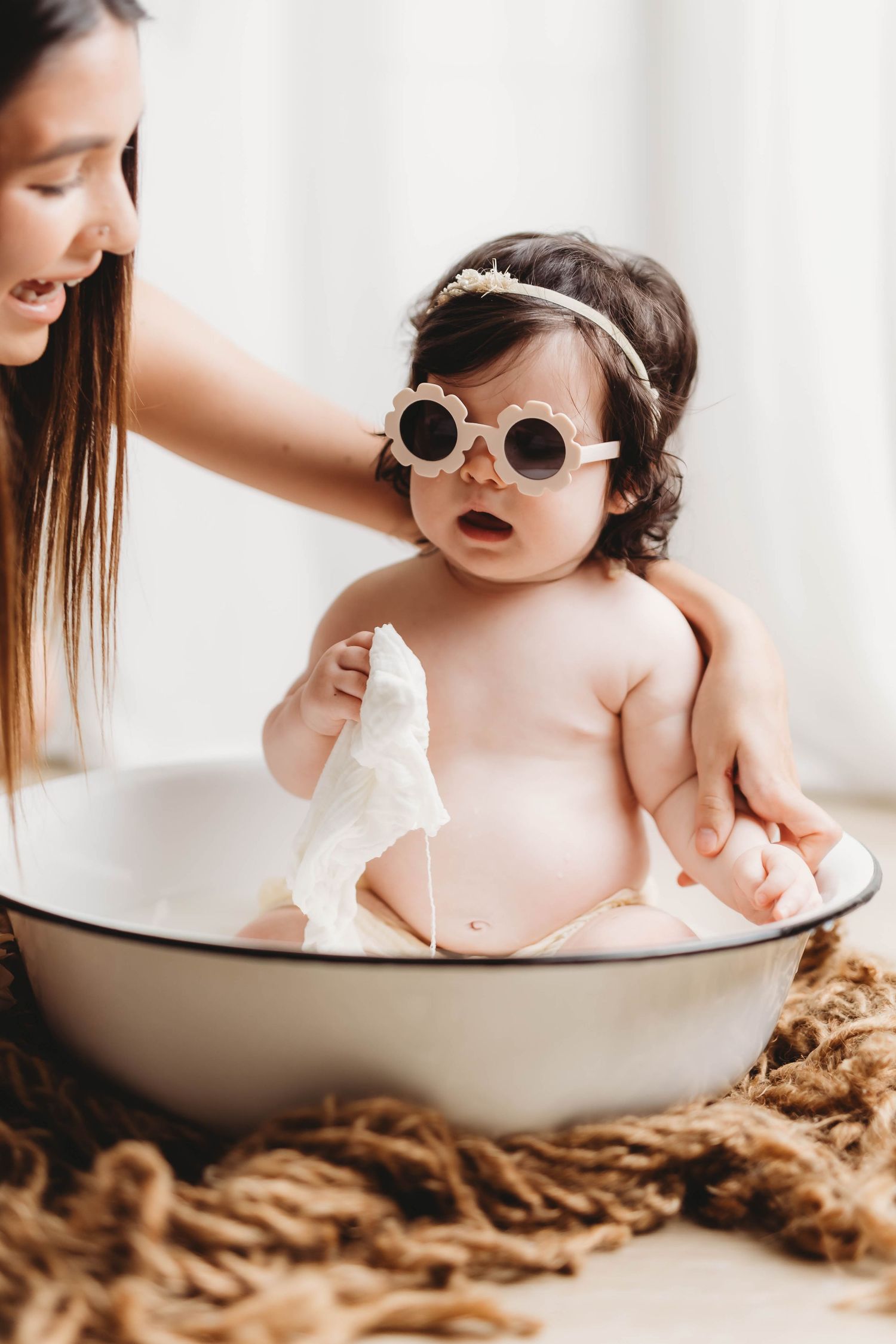Playful baby wearing white sunglasses during milk bath photography session.