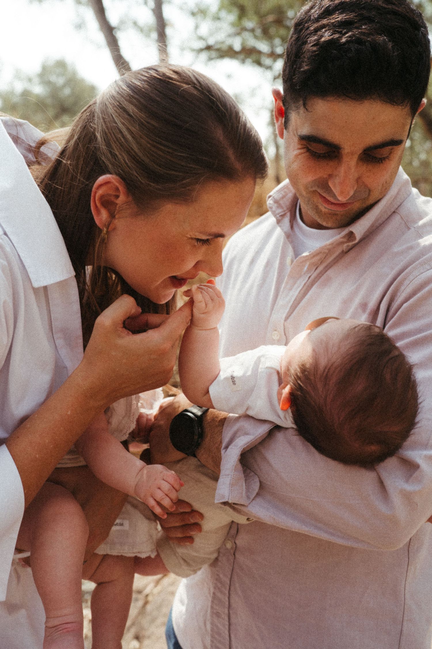 Parents share tender moments with their newborn baby while wearing white clothing outdoors.