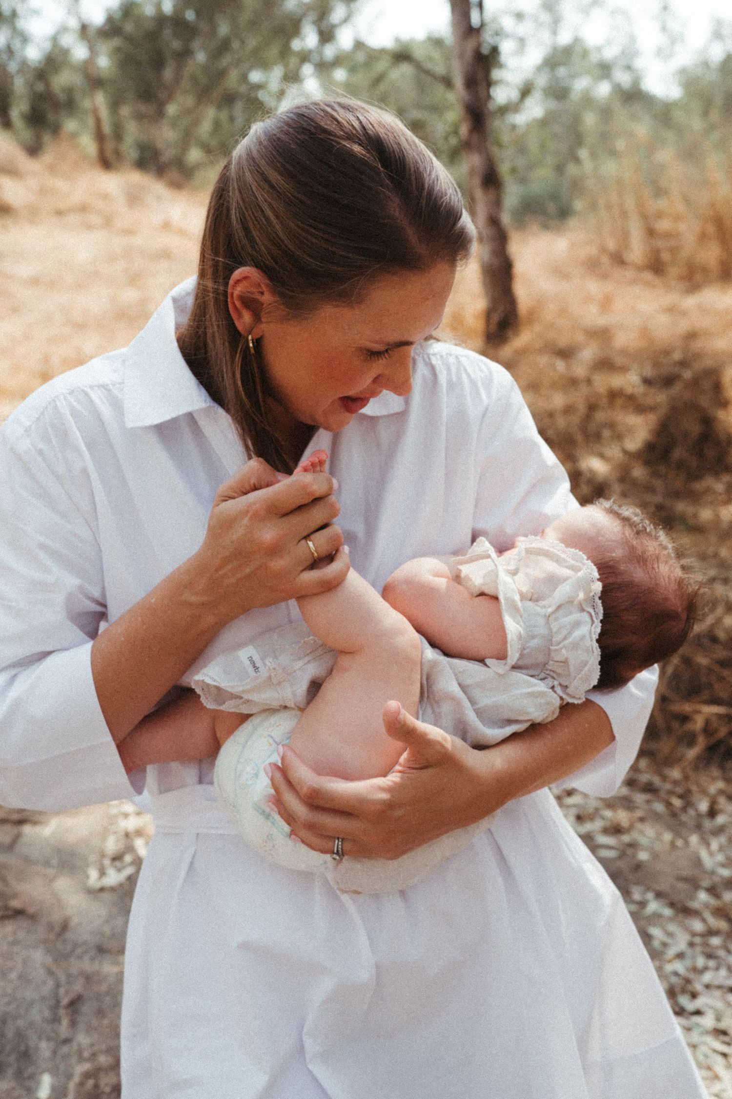 Parents in white clothing share intimate moments with their baby in an outdoor setting.