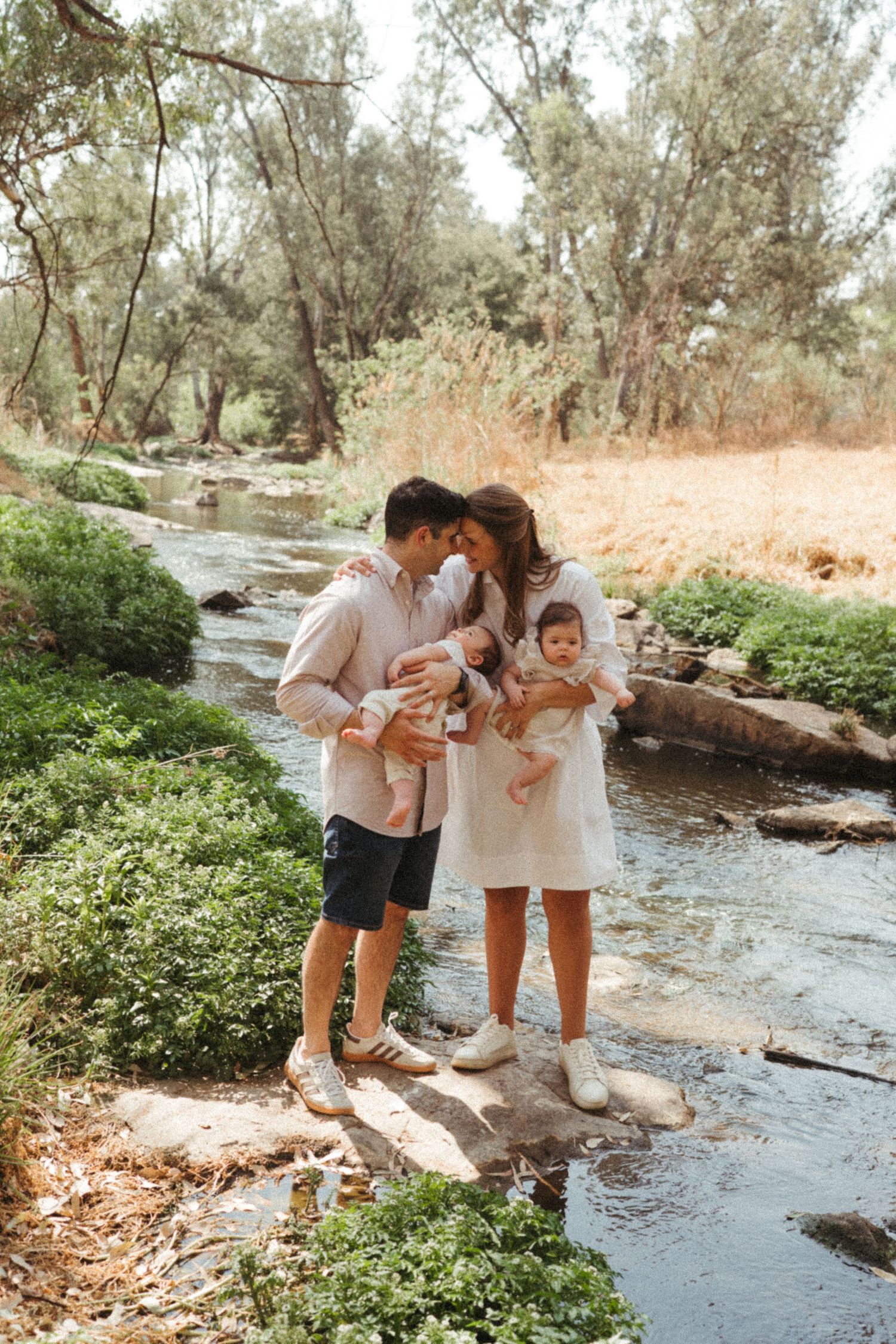 Family exploring together by a creek in matching white outfits on a sunny day.