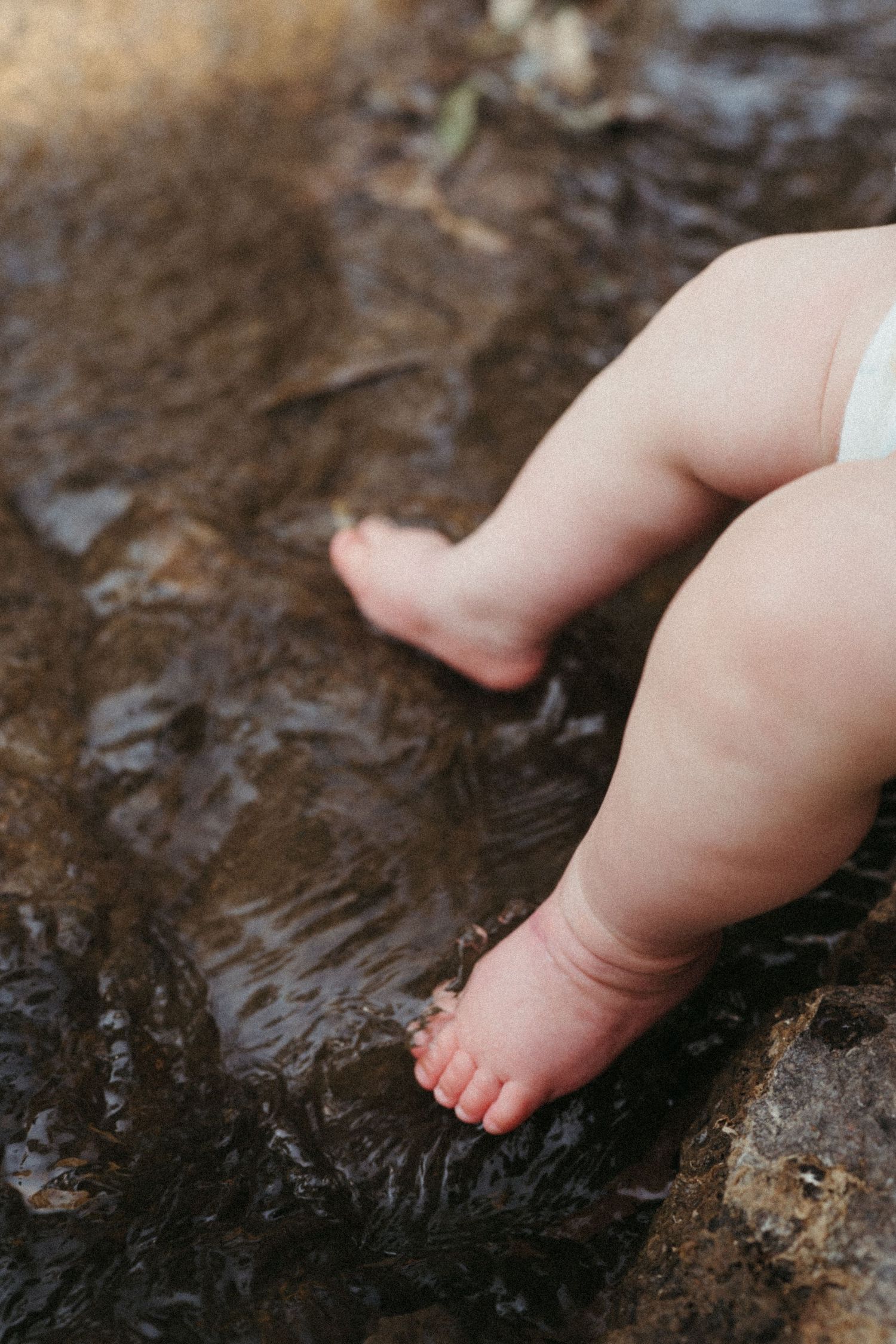 Close-up of tiny baby feet touching water in a natural stream.