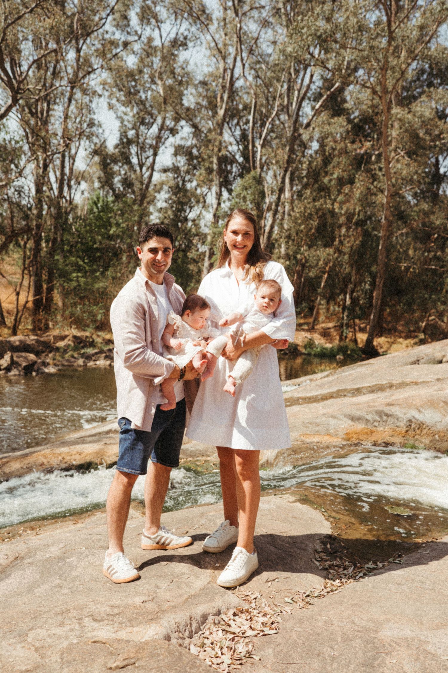 Family in white clothing spending time together near a rocky creek on a sunny day.