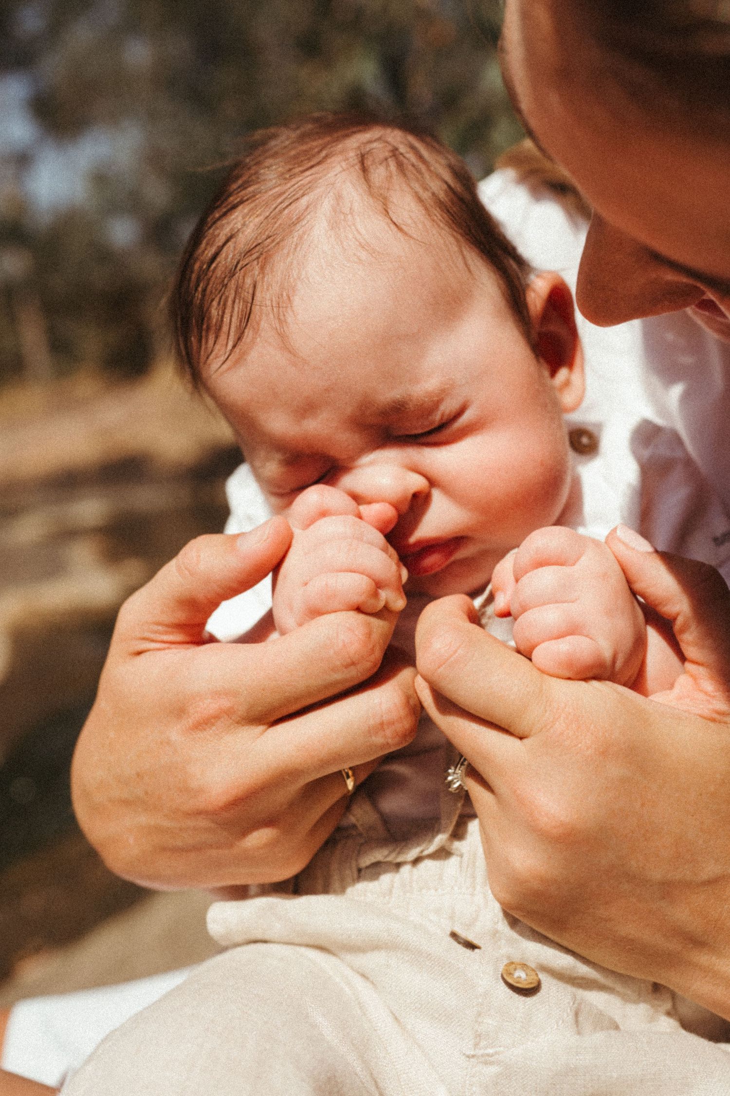 Close-up of tiny baby hands being held against a natural outdoor background.