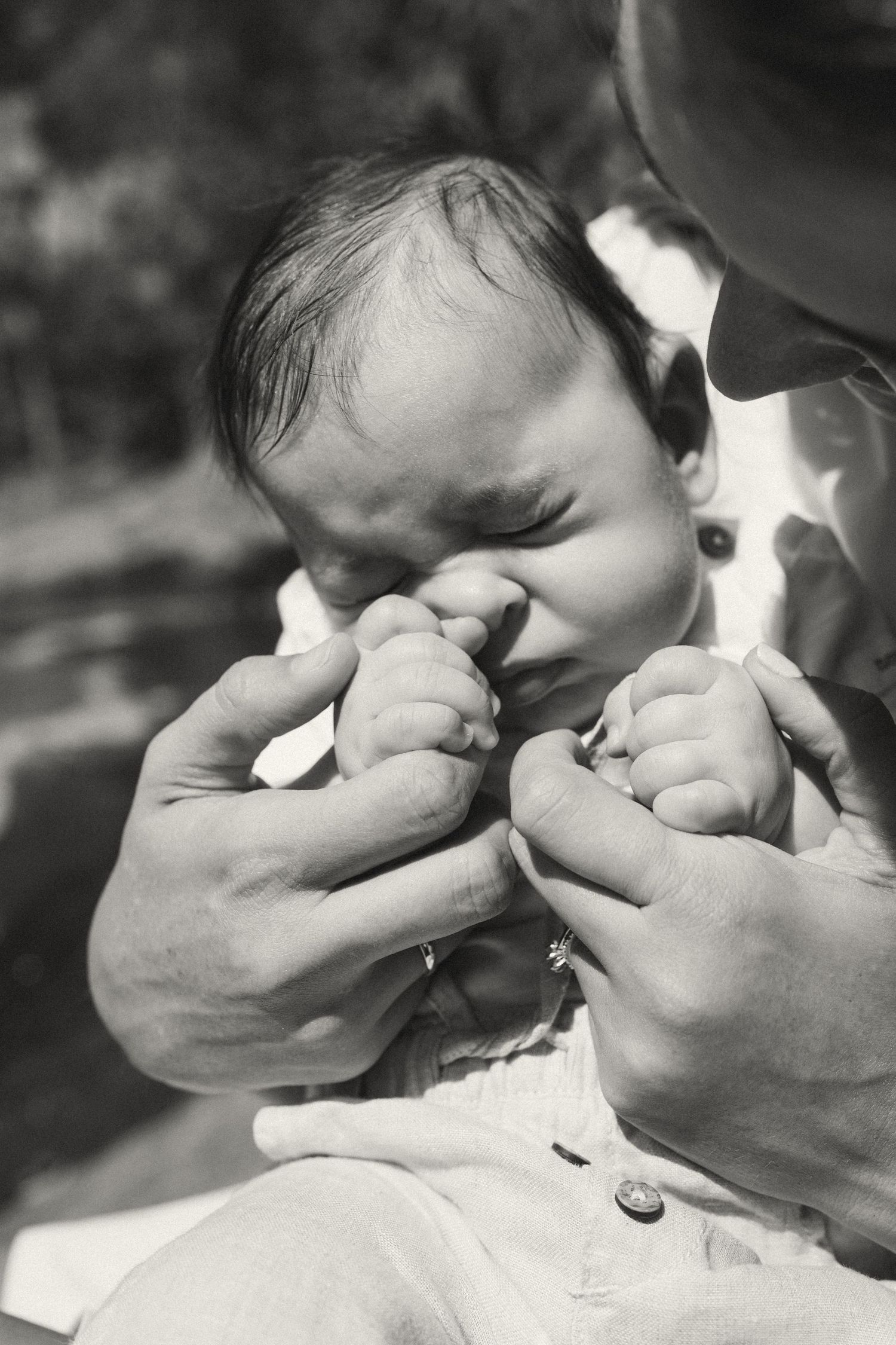 Black and white close-up of a baby's face with hands reaching from off-frame.