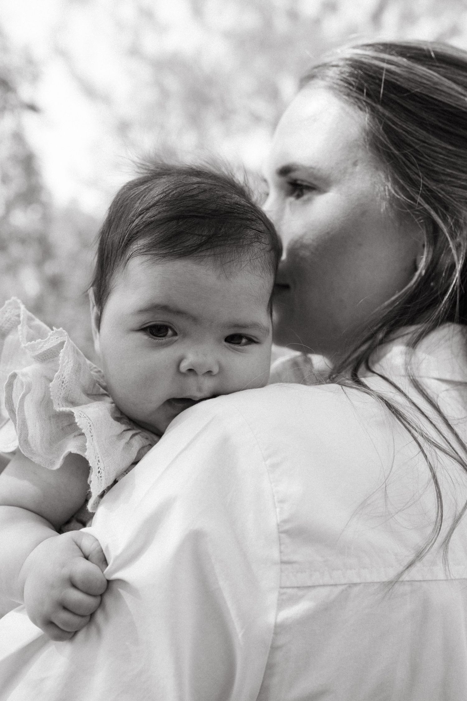 Black and white portrait of tender moment between parent and baby in white clothing.