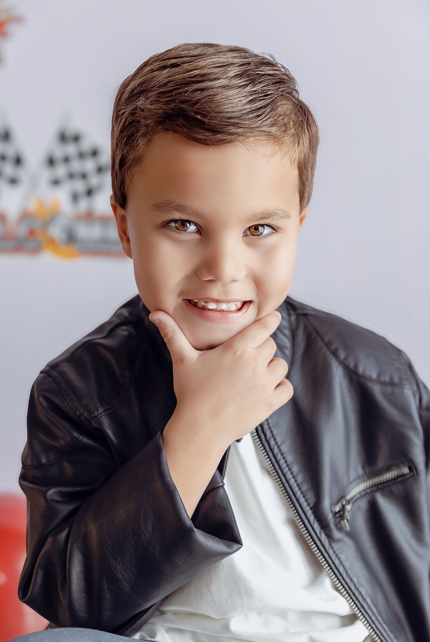Imagen de cercania de nino con la mano en la barbilla posando para fotografias profesionales utiliza una chaqueta de cuero.