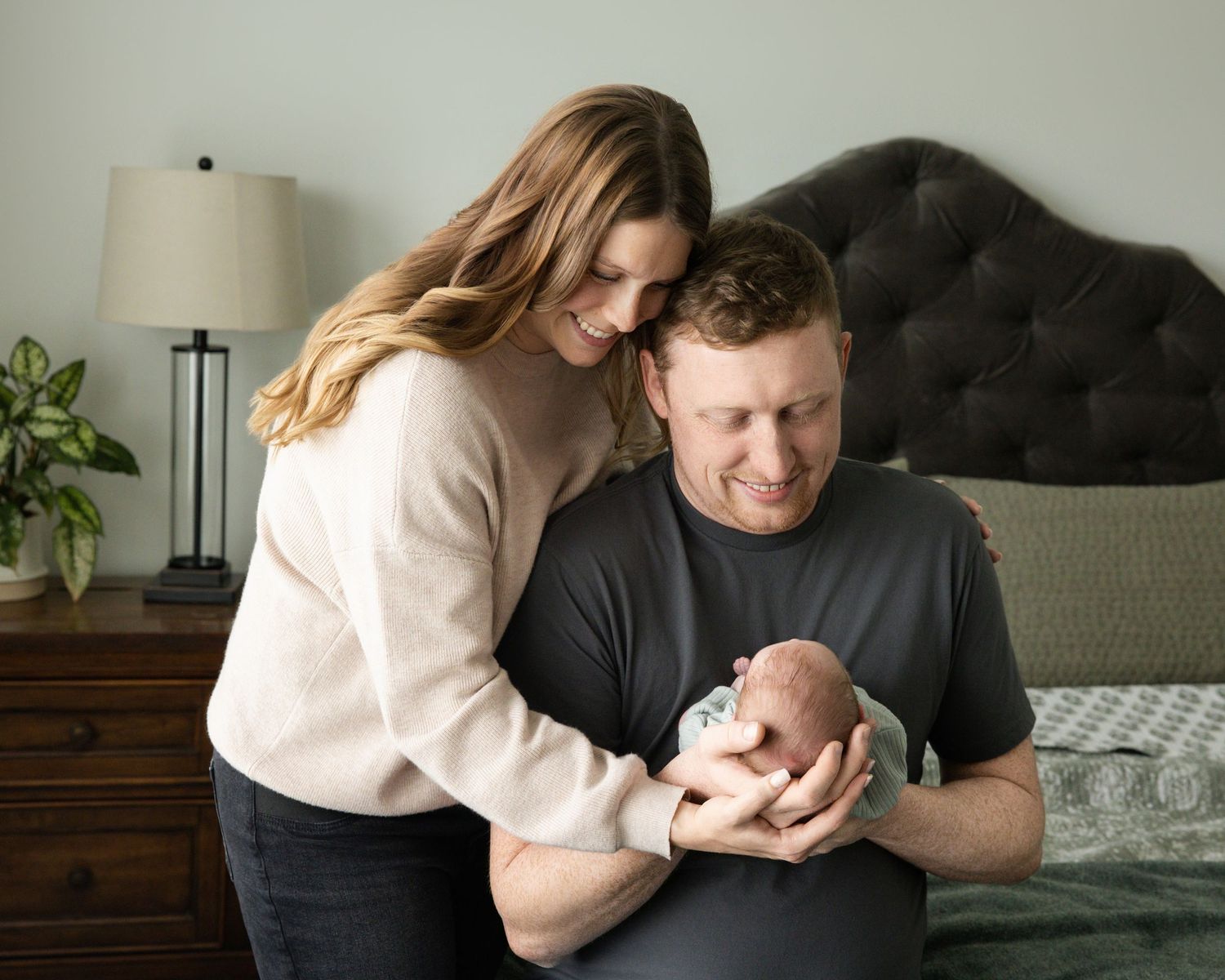 A couple in casual attire shares tender moments with their newborn baby in a cozy home setting.