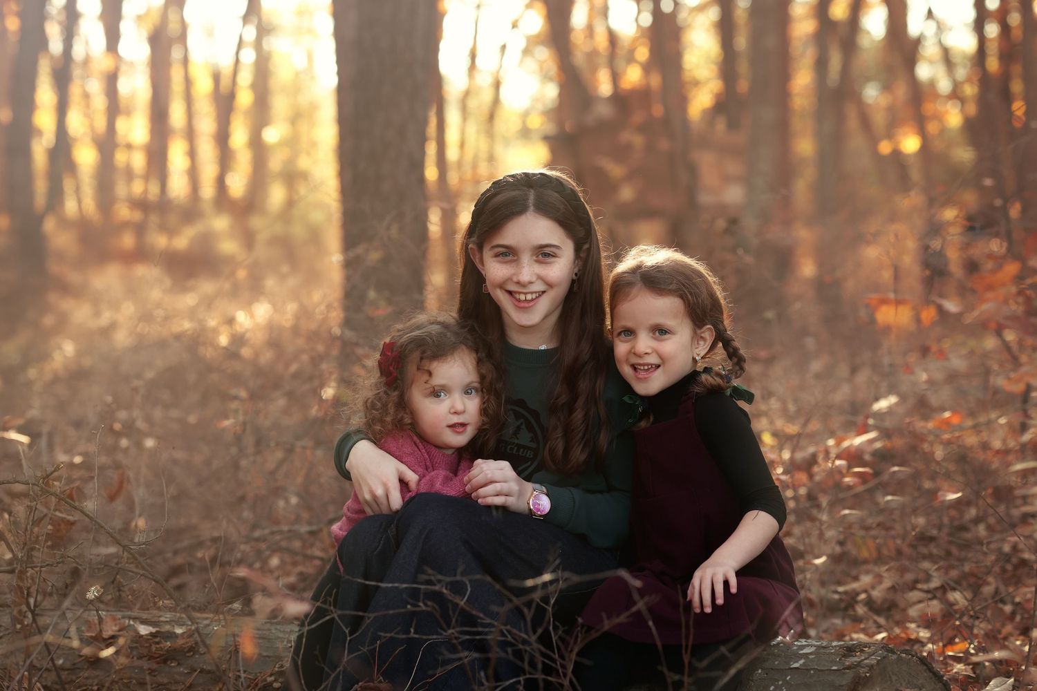 Three sisters sitting together for a golden hour fall photography session in the woods