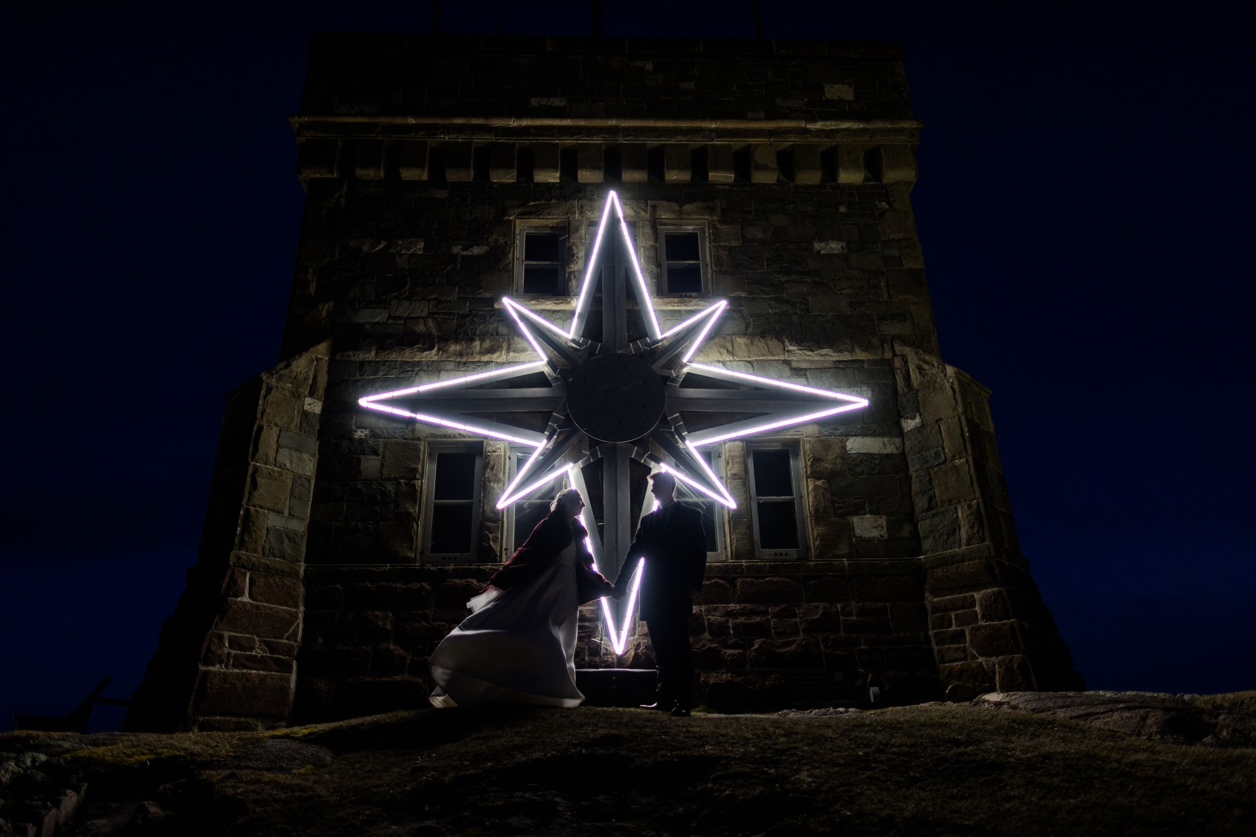 Illuminated star-shaped Christmas lights mounted on a brick building facade at night.