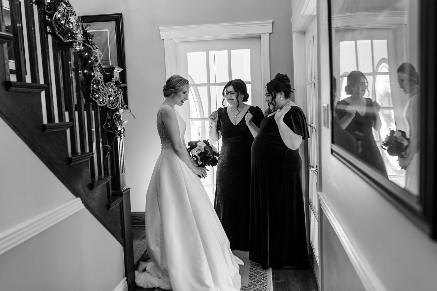 A series of black and white wedding preparation photos showing dress adjustments and intimate moments in a bright room.