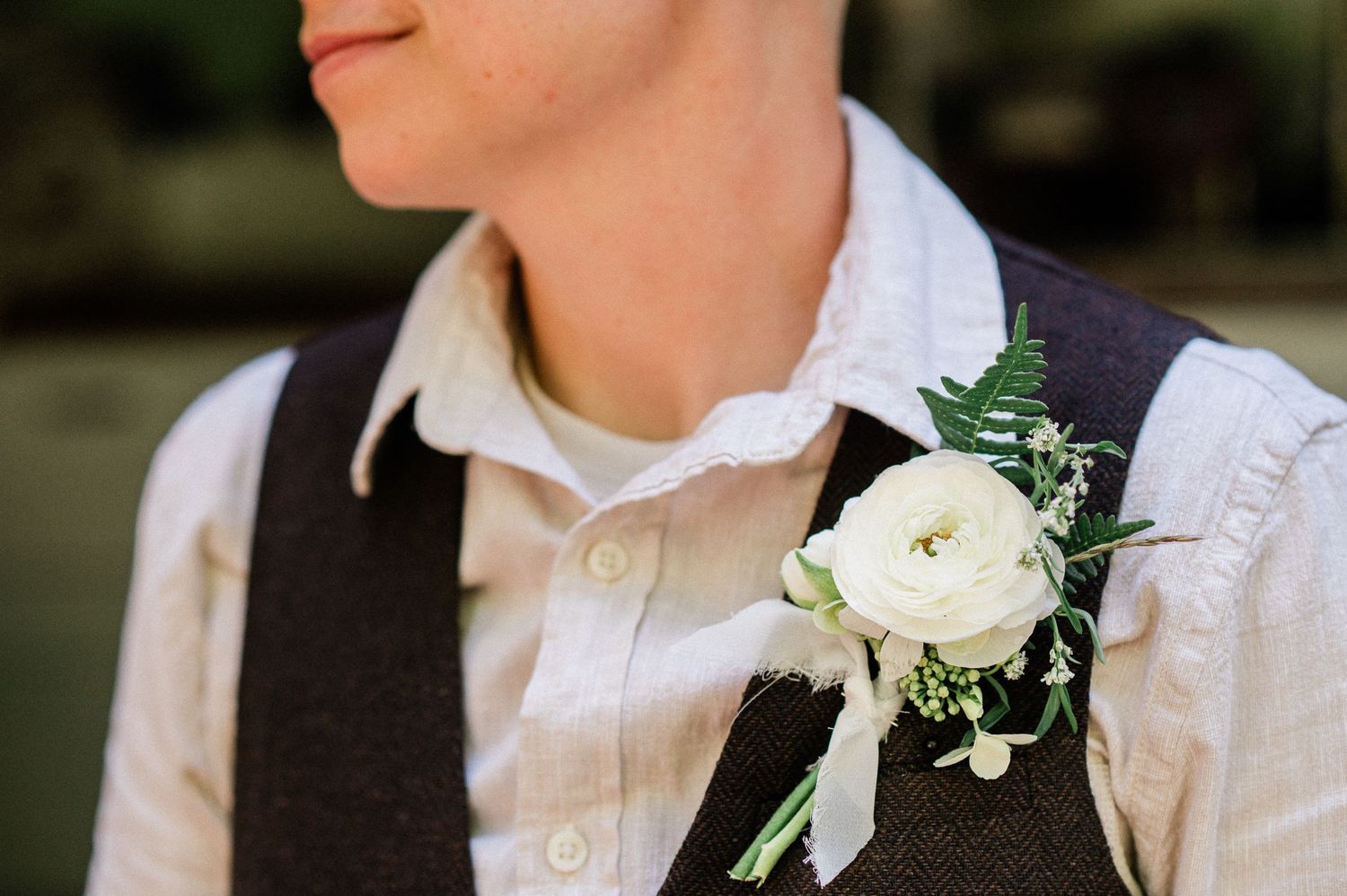 A close-up view of white floral boutonnieres with delicate greenery pinned to formal wedding attire.