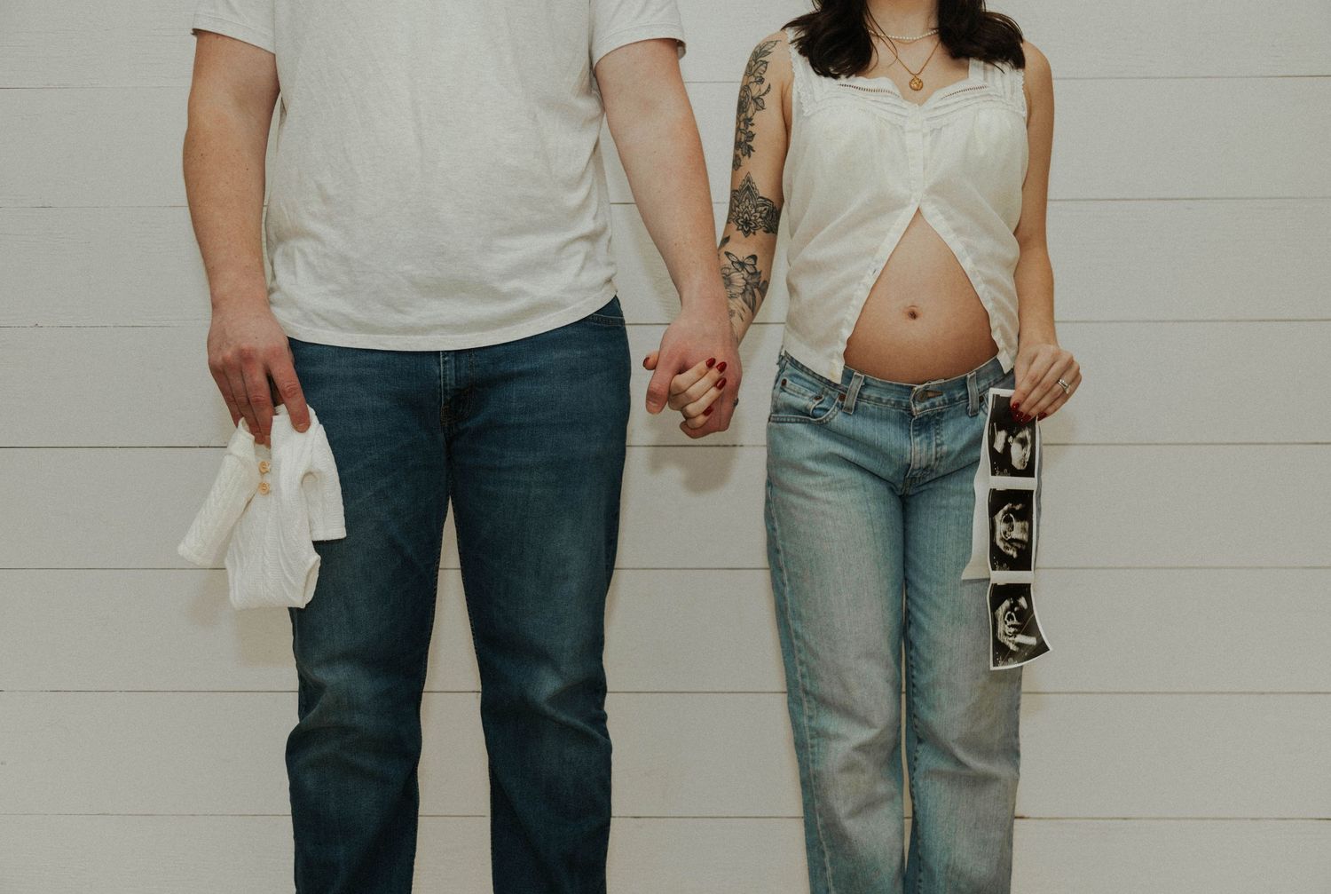 Expectant couple holding hands, woman's pregnant belly visible in cropped photo.