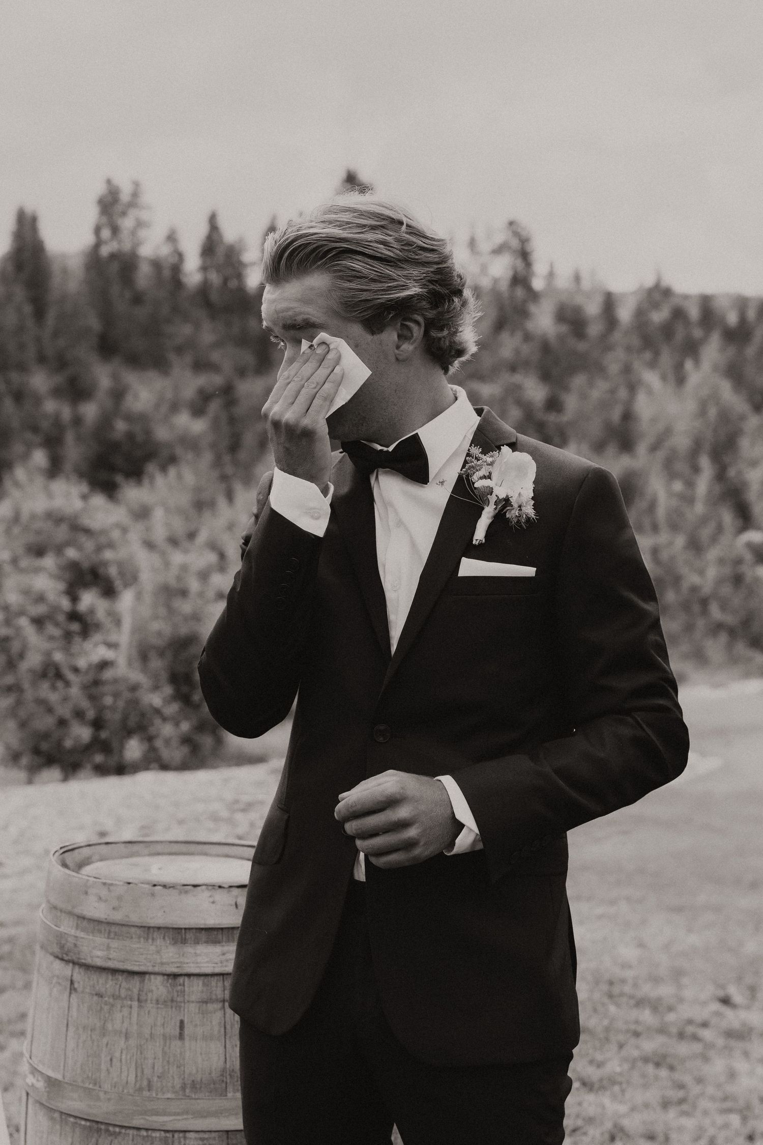 Close-up of a bride's hand with wedding ring resting on groom's back in an intimate black and white moment.