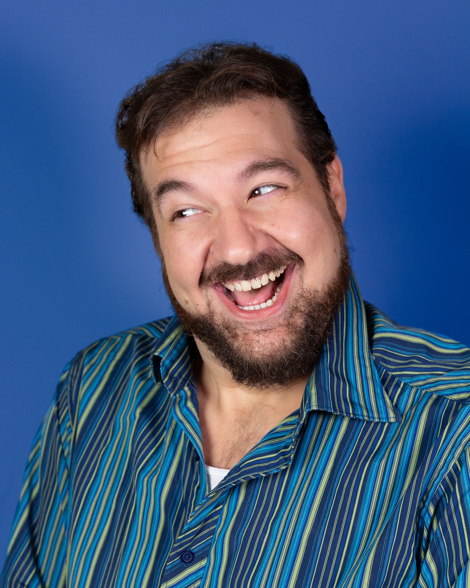 Headshot photography: a man against a blue backdrop wearing a striped shirt and laughing