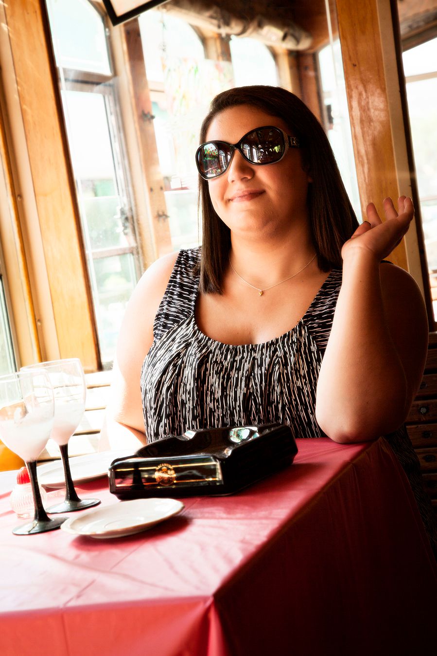 A person wearing sunglasses and a black and white patterned top sits at a restaurant table with a red tablecloth. (Bergen New York)