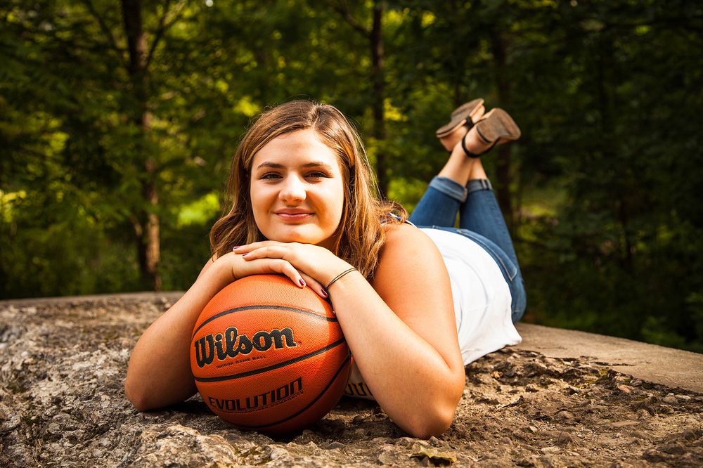 A basketball player relaxes on a rock in a forest setting, with a Wilson basketball beside them. (Gates New York)