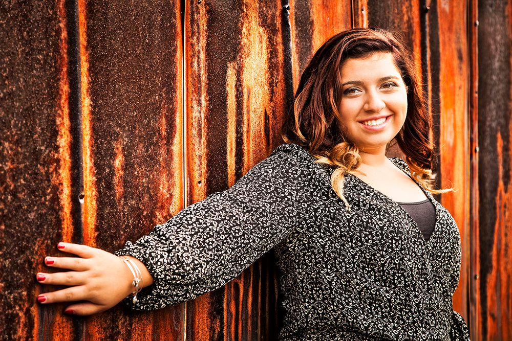 A smiling person in a polka dot dress poses against a rustic wooden background with warm lighting.