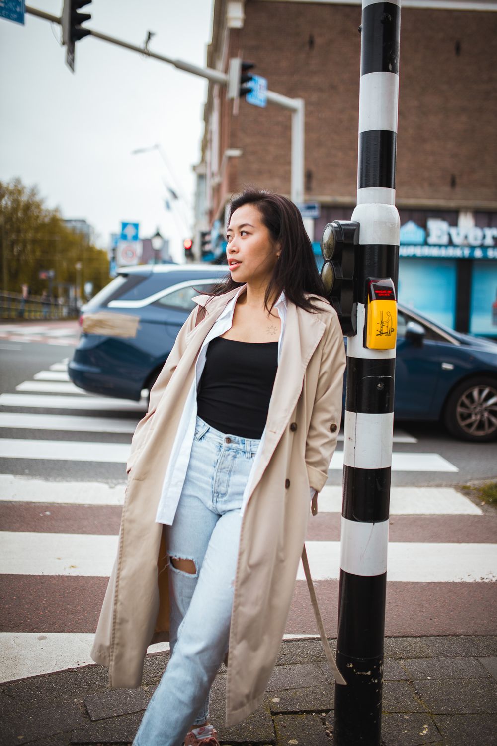 Stylish street fashion look featuring light beige trench coat paired with light wash denim and black top in urban setting.