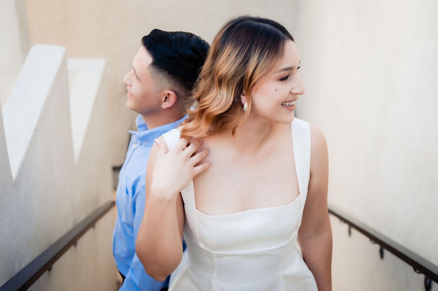 A couple in wedding attire shares a joyful moment while standing on concrete stairs.