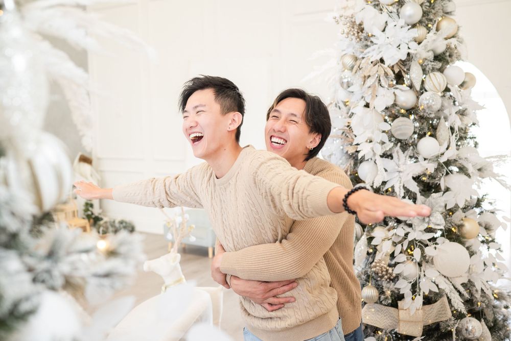 Two people sharing a joyful laughing moment in front of white Christmas trees.