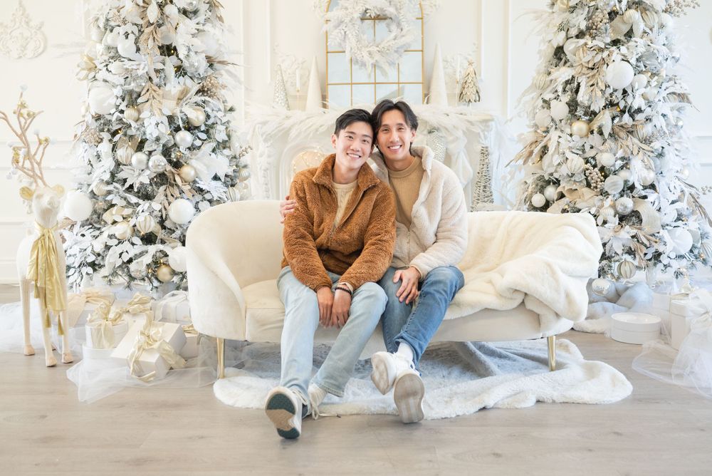 Two people in casual wear sitting together on white couch with Christmas trees in background.