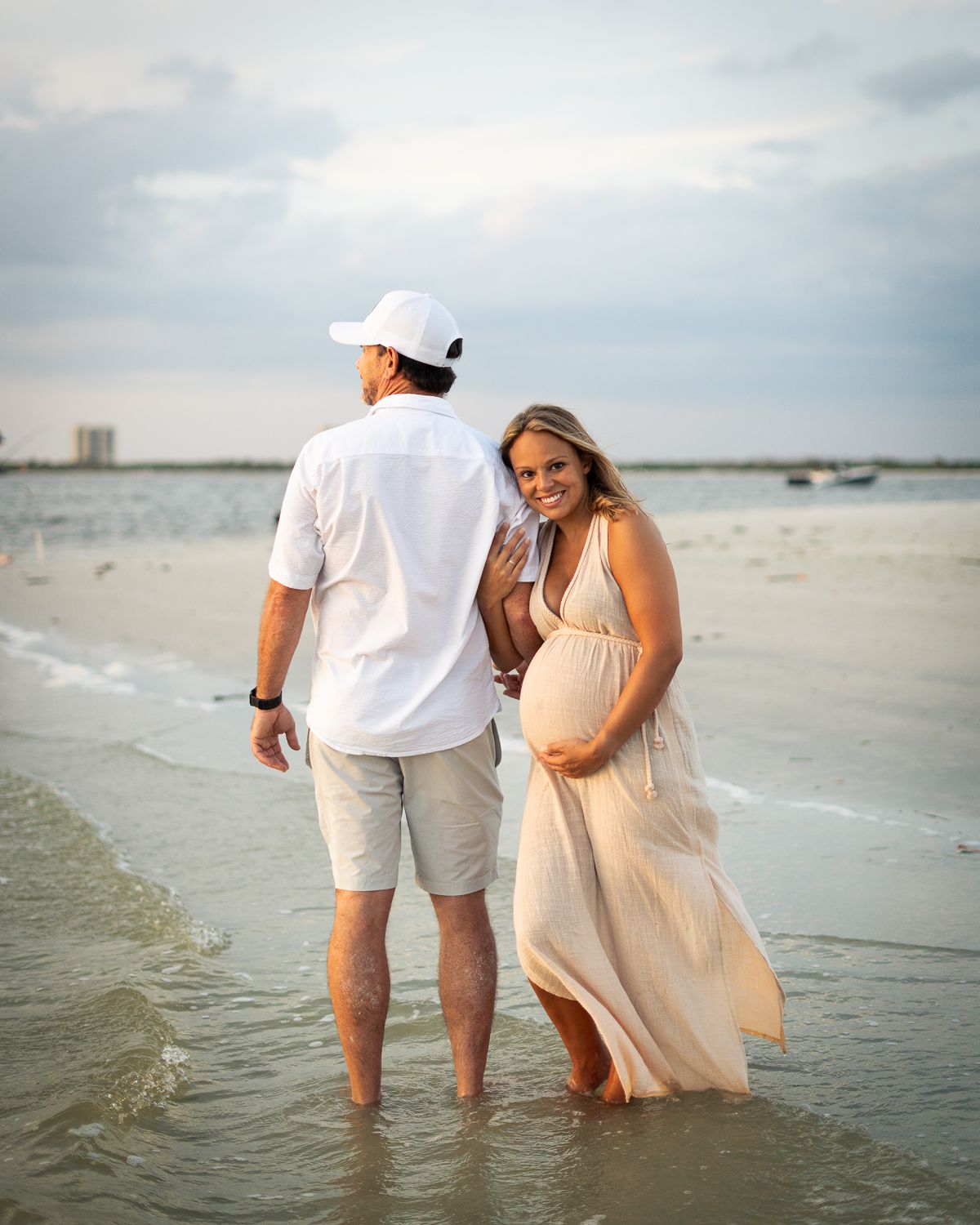 A romantic beach photoshoot with people wading in shallow water during golden hour.
