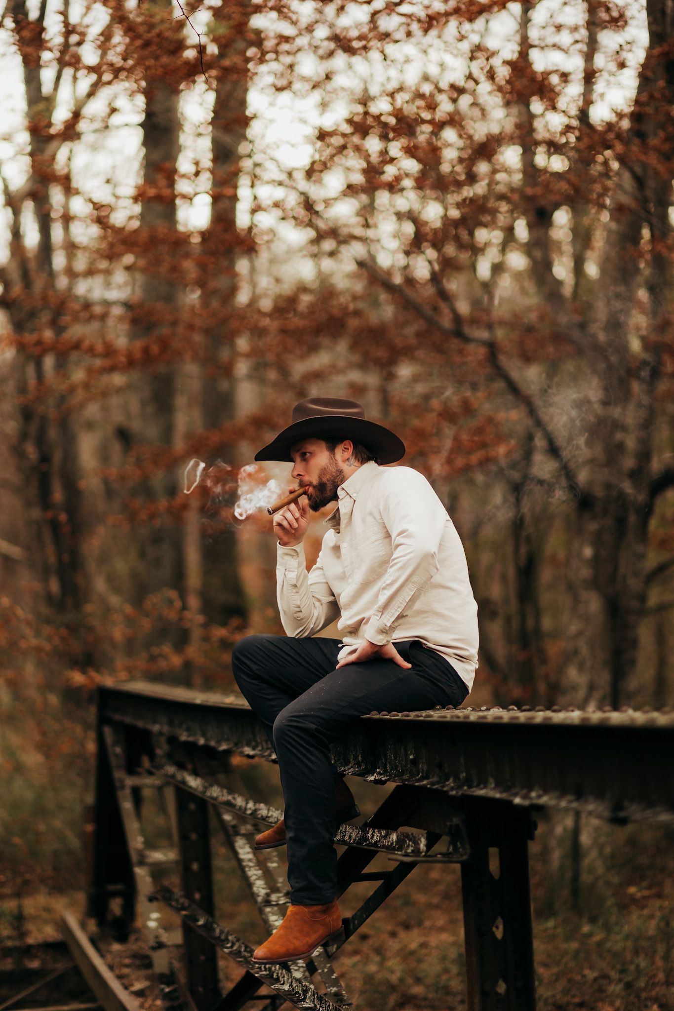 man with a cowboy hat sitting on a bridge smoking a cigar