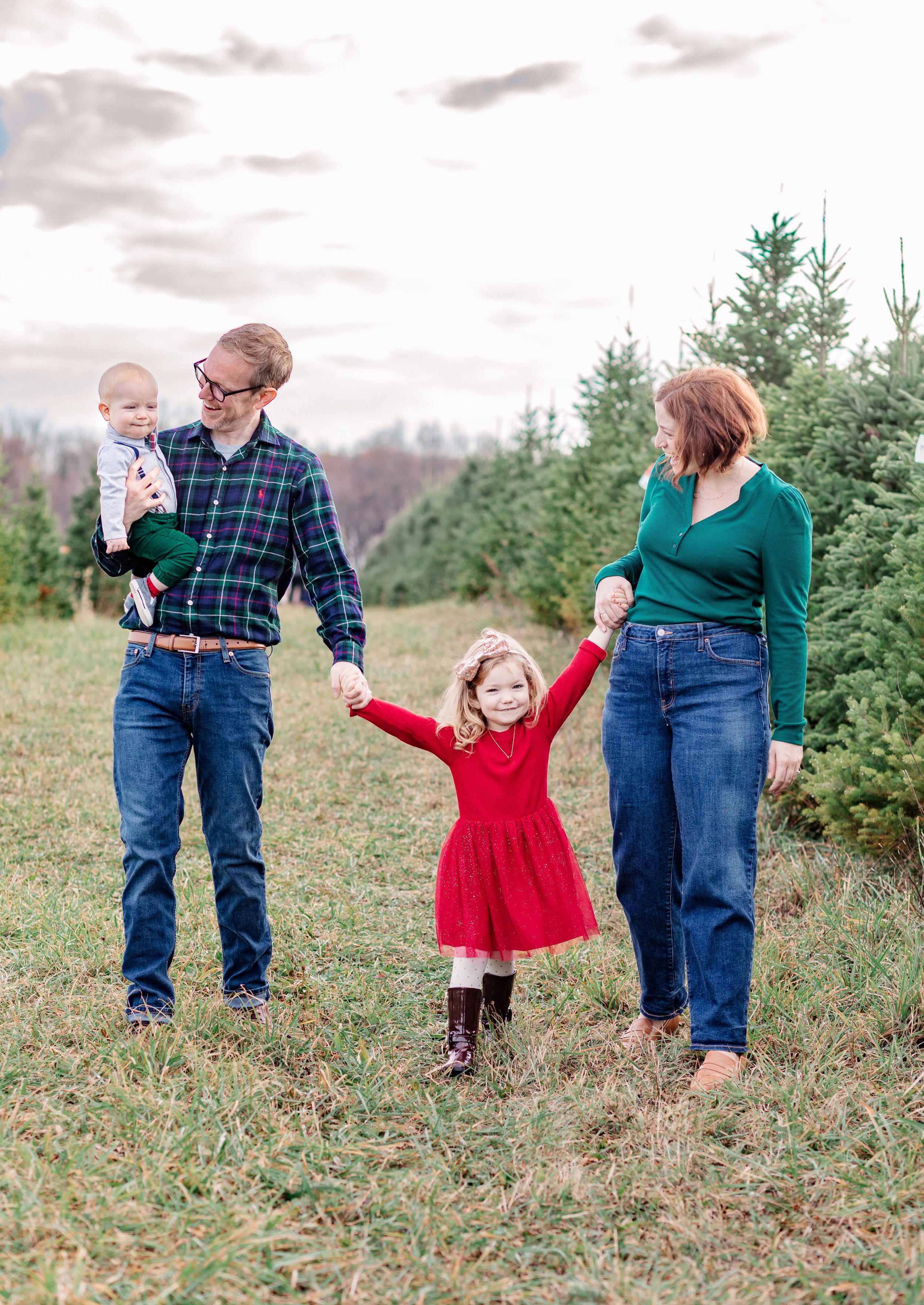 A family poses together at a Christmas tree farm wearing coordinated green and red outfits on a cloudy day. Location Mason, Michigan