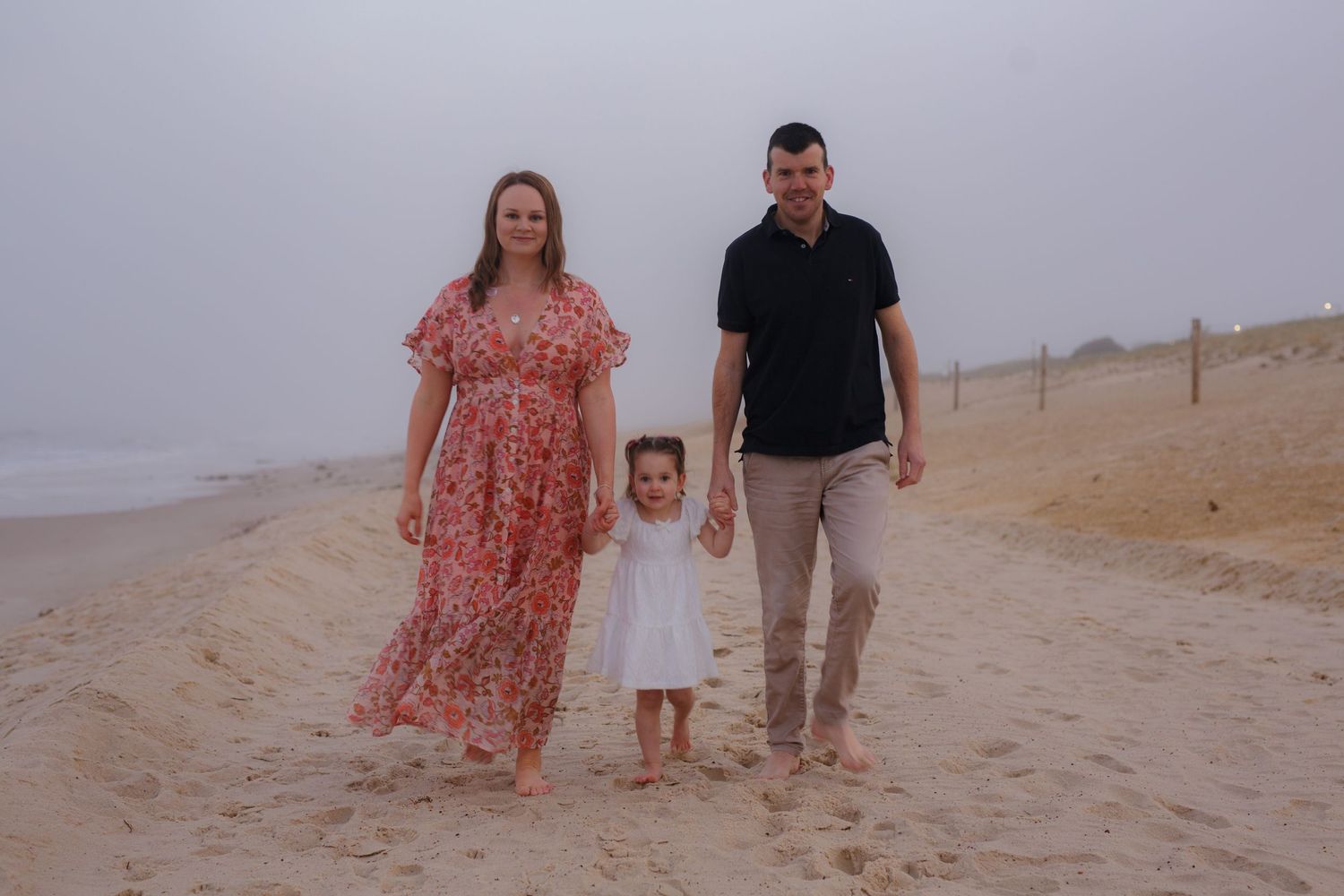 A family walks together on a misty beach with soft overcast lighting.