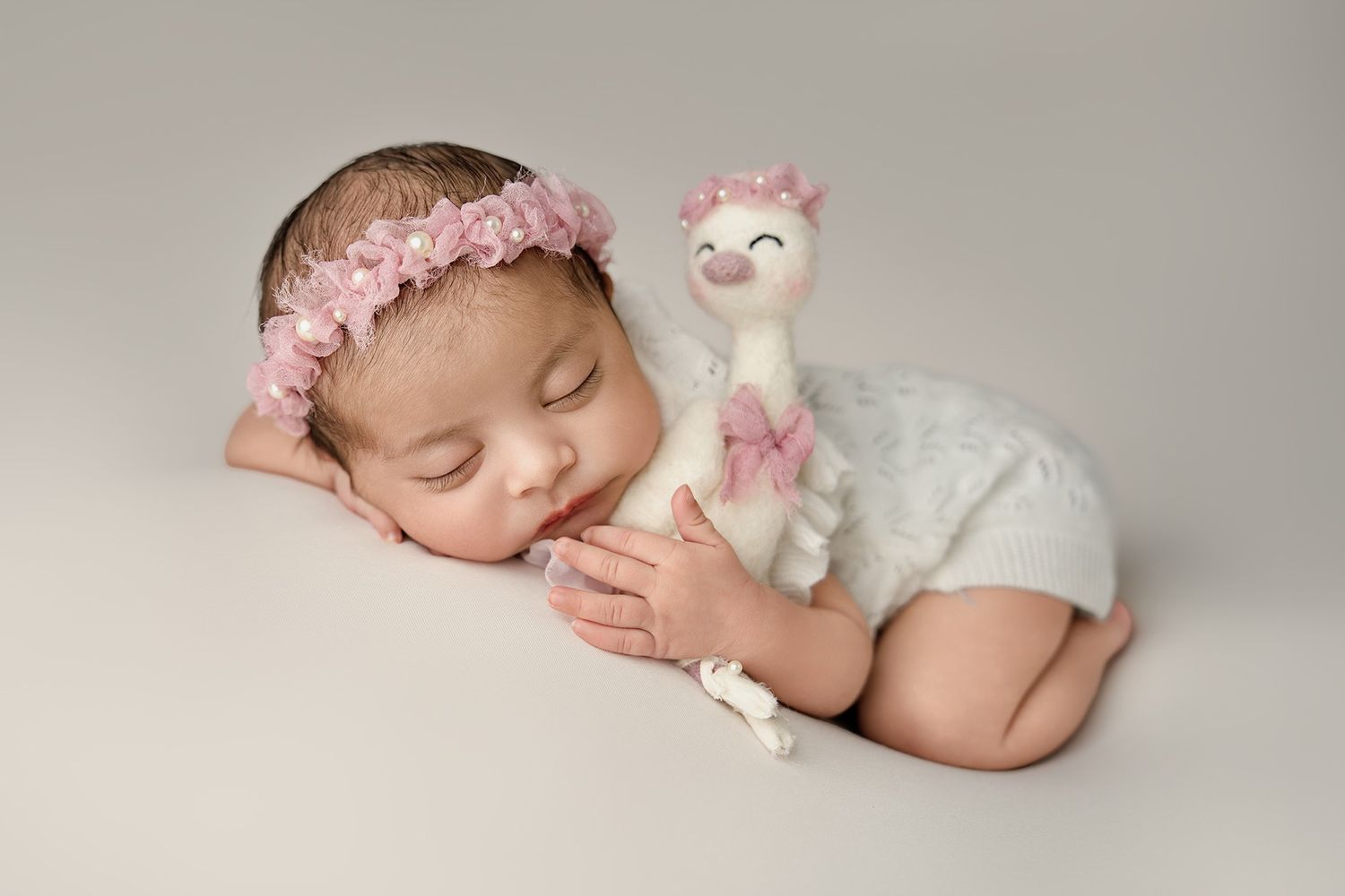 Newborn photography series with baby wearing pink headband and white wrap on neutral backdrop.