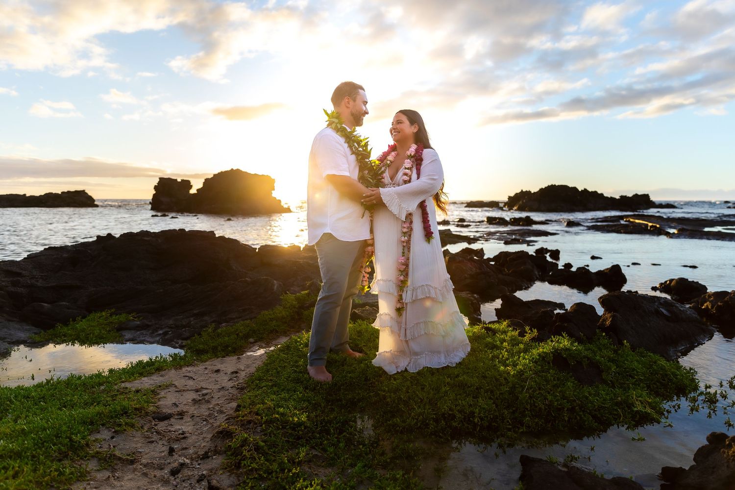 A romantic sunset wedding portrait on a rocky beach coastline with golden light streaming through the clouds.