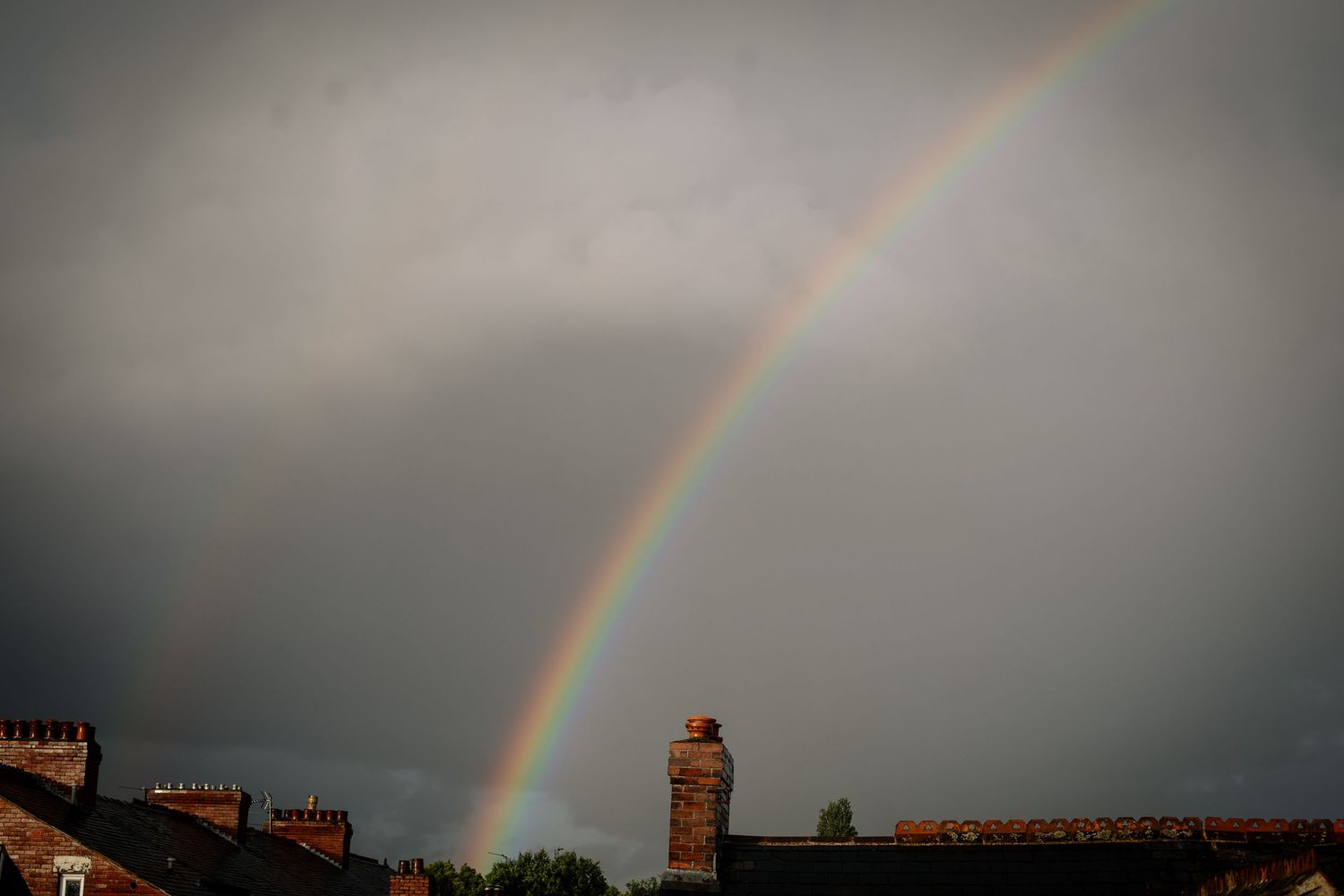 Vibrant double rainbow arches over rooftops against a moody grey sky.