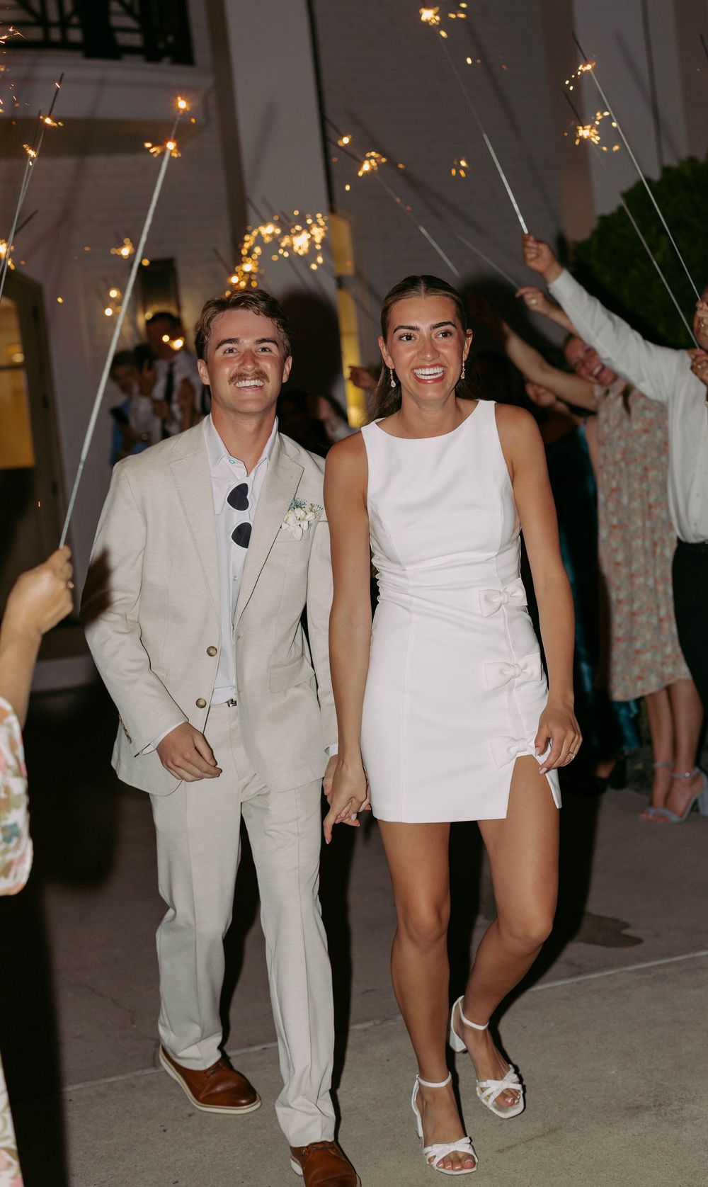 A couple stands together at an evening celebration with sparklers twinkling in the background.