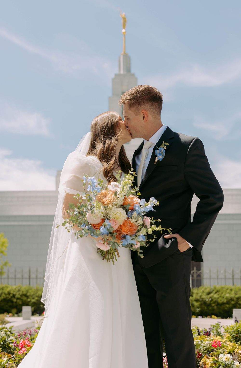 A couple shares a romantic moment in a garden with blooming flowers and a beautiful bouquet on their wedding day.