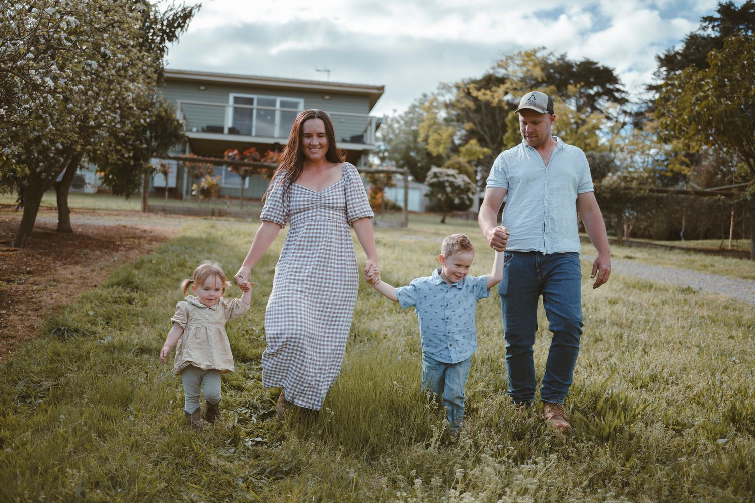 Family walking together on grassy hill with house in background.