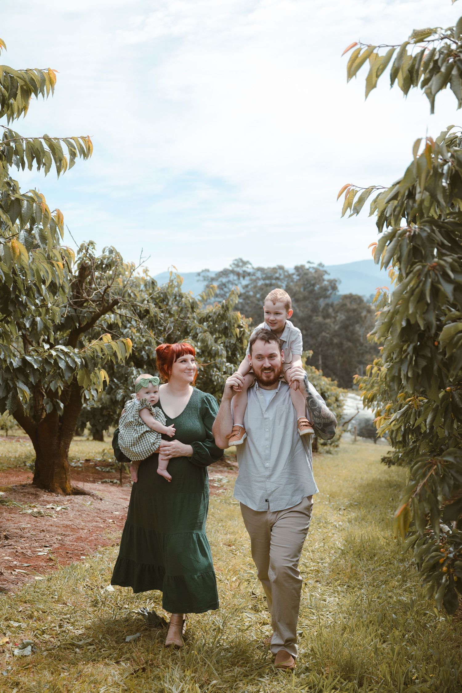 A couple playfully walks and poses together in an orchard on a sunny day, surrounded by fruit trees.
