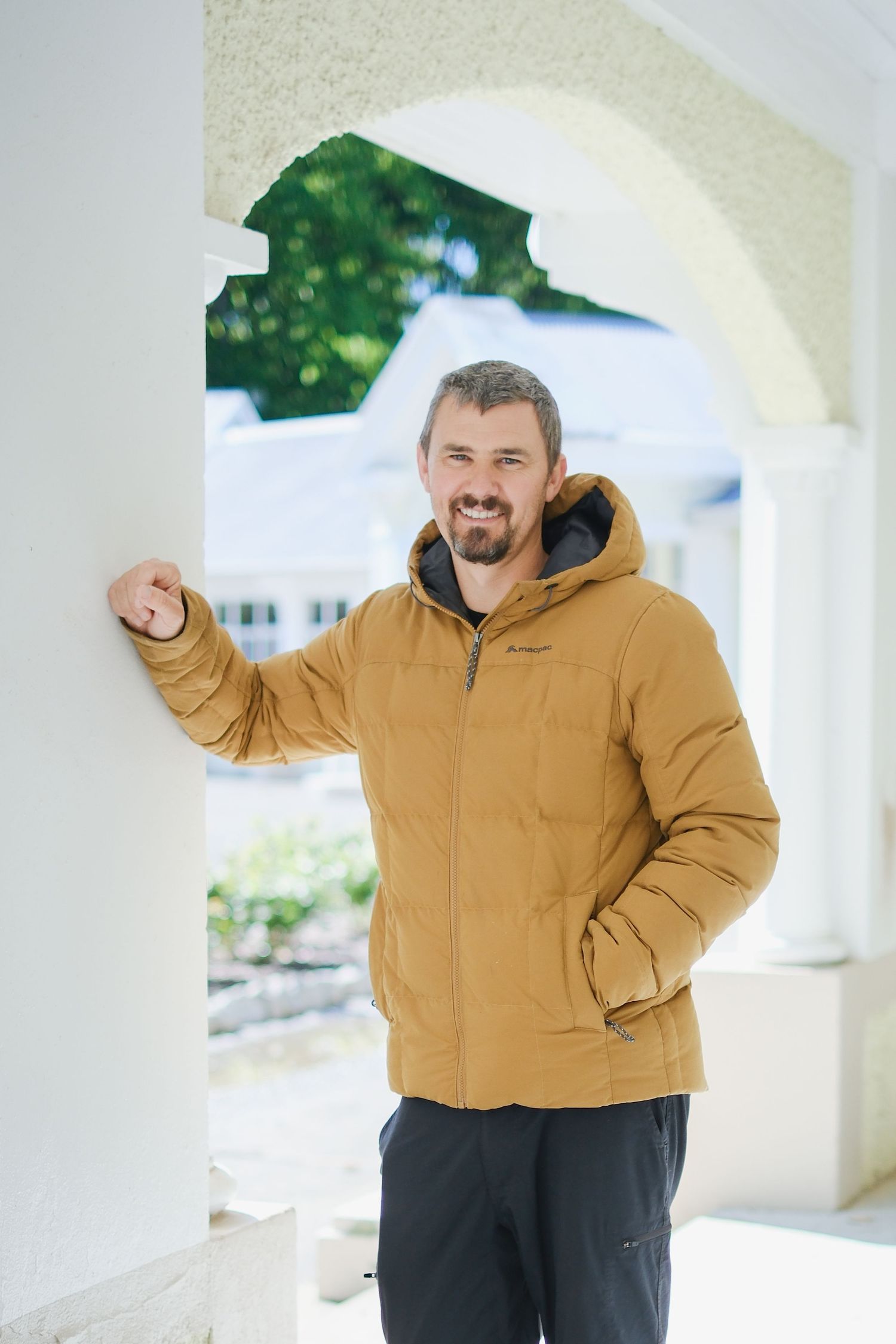 Person in yellow winter jacket standing under white archway outdoors.