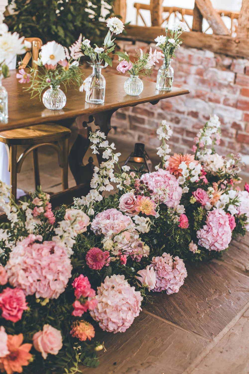 Elegant floral table decorations featuring pink hydrangeas and hanging glass vases at a rustic brick venue.