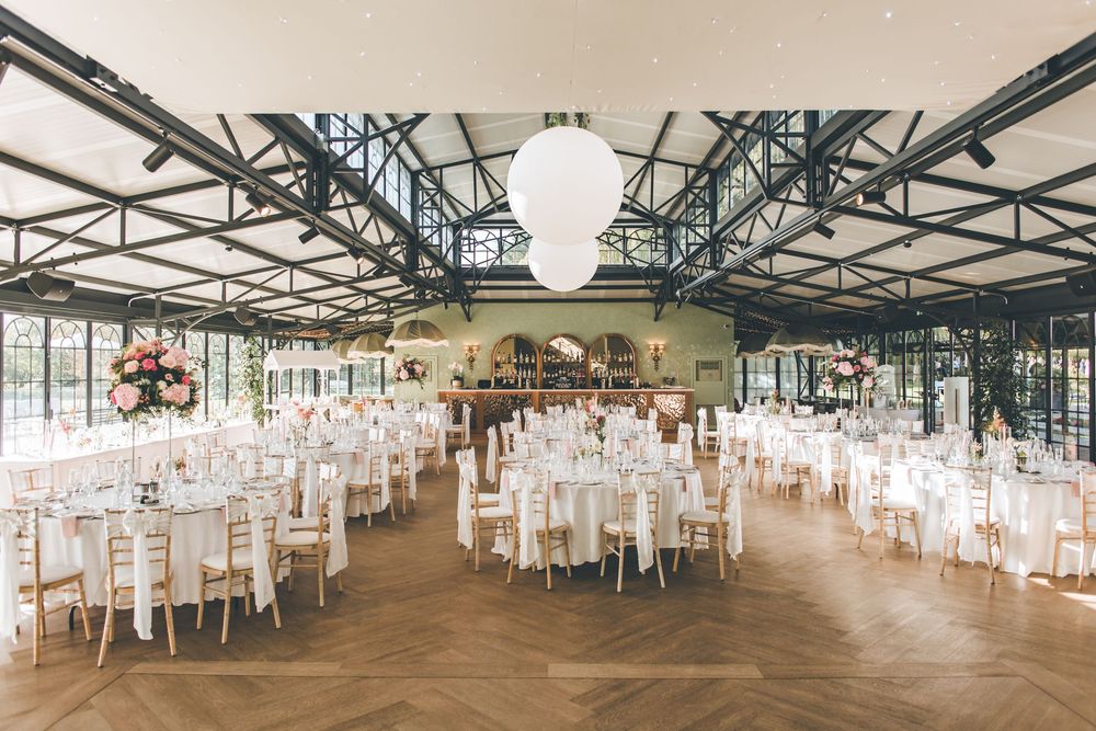 Panoramic view of an empty wedding reception hall with white tables and industrial ceiling beams.