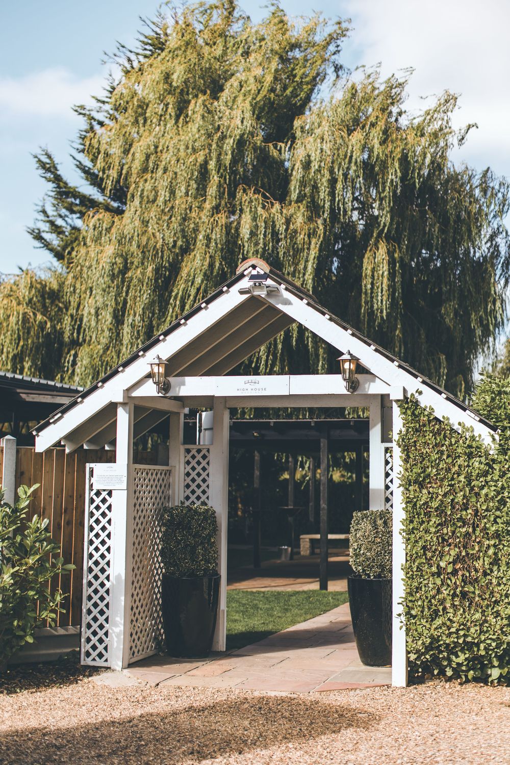 A white wooden wedding arch entrance with lattice details framed by a majestic weeping willow tree.