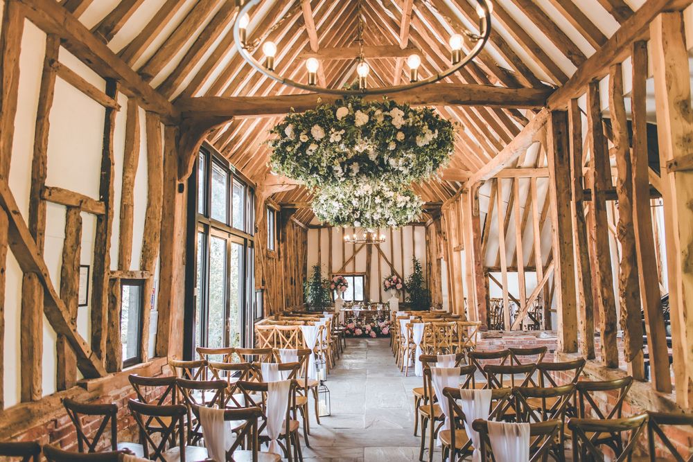 Rustic barn wedding venue with wooden beams and hanging greenery chandelier set up for ceremony.