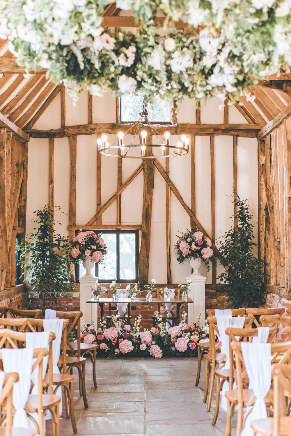 Rustic barn wedding venue with wooden beams decorated in white flowers and pink accents.