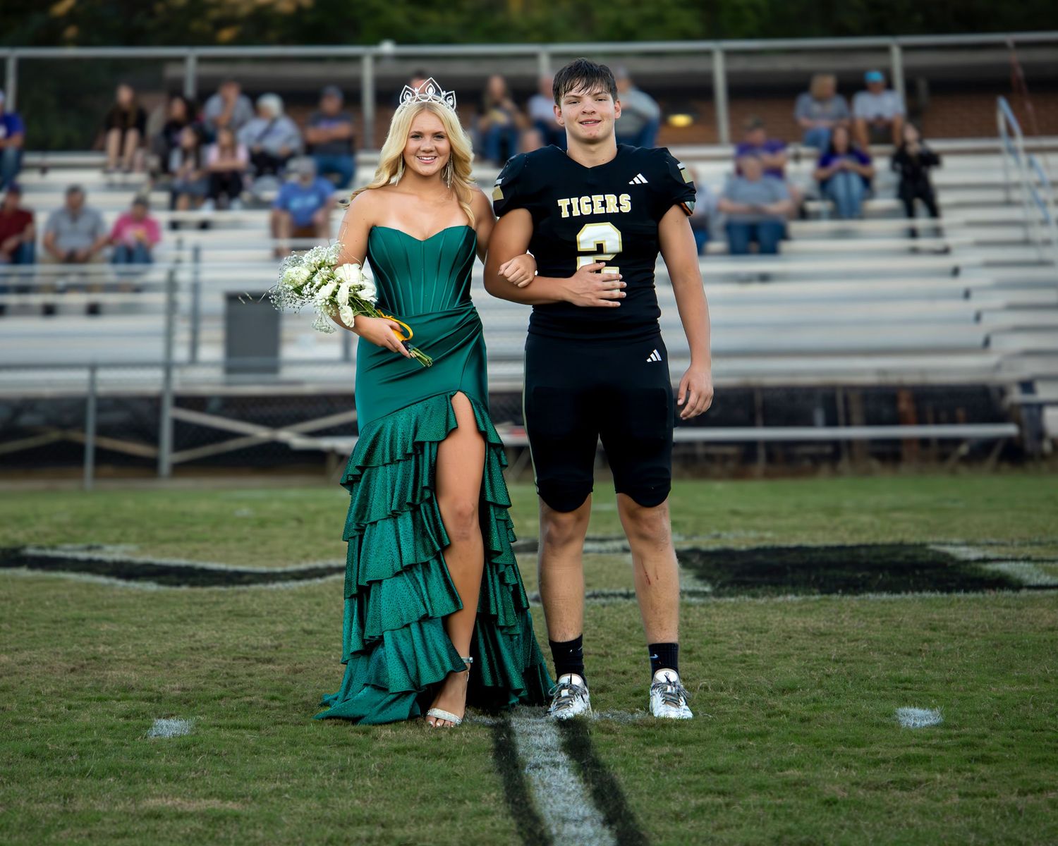 Two people in formal attire run across a grass field during what appears to be a homecoming event.