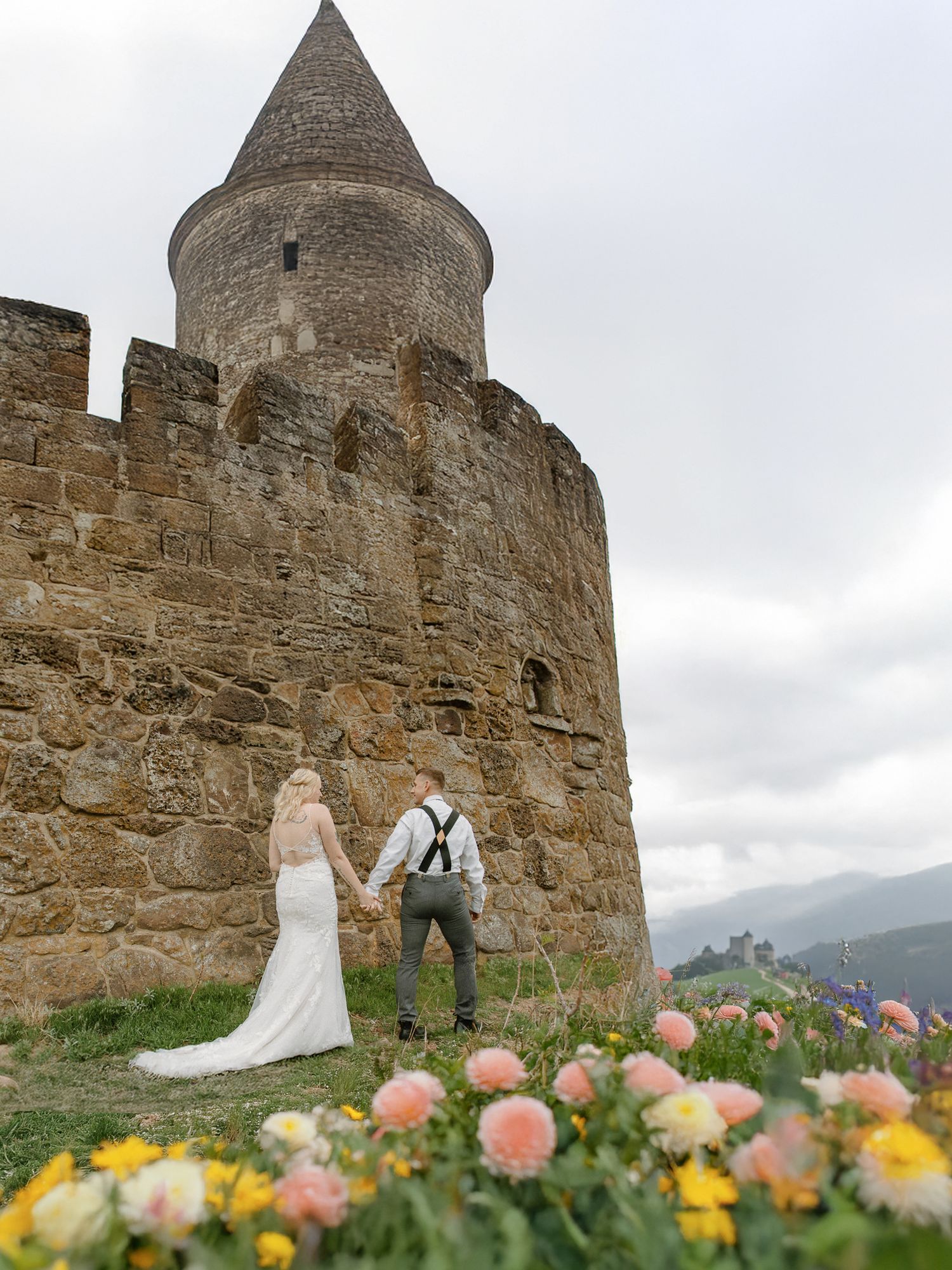 A couple shares an intimate moment on a hilltop overlooking a vast green countryside landscape on their wedding day.